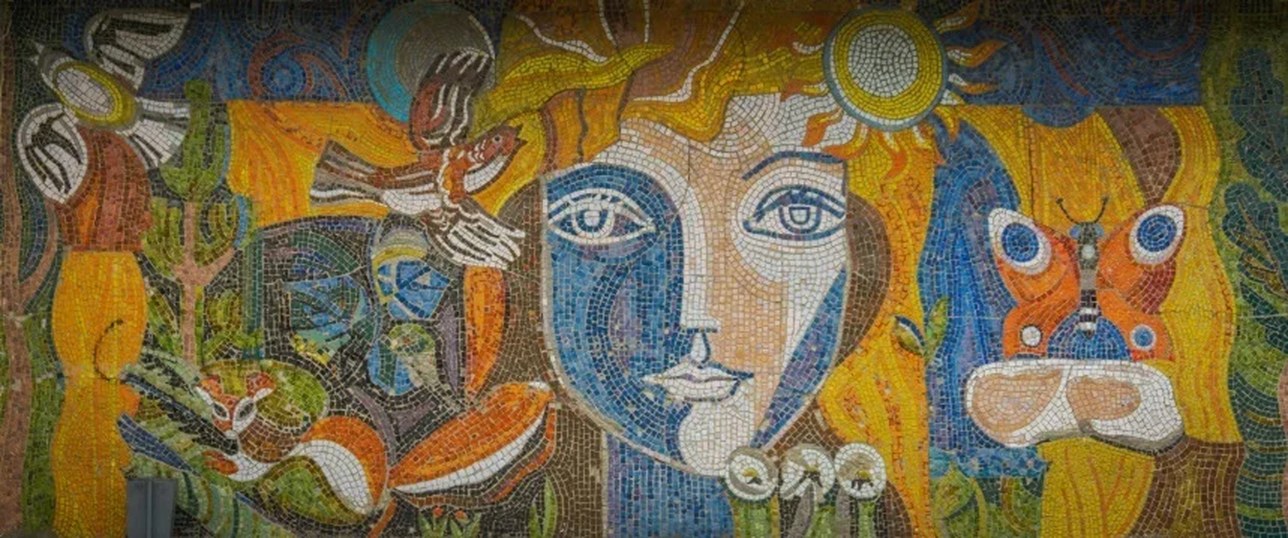 Деталь панно вблизи: лицо, солнце, птица и бабочка выложены смальтой